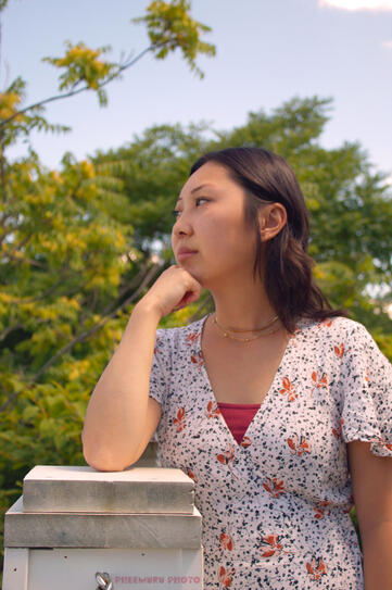 Headshot of Abbie Van Lee with a warm undertone. Looking to the left with her hand on her chin.
