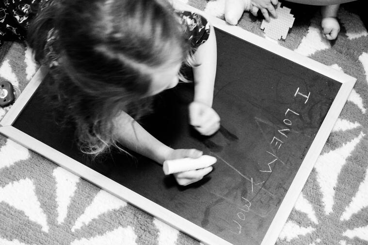 The eldest sister is propped up on her elbows on a blackboard. She wrote "I LOVE My MOM"